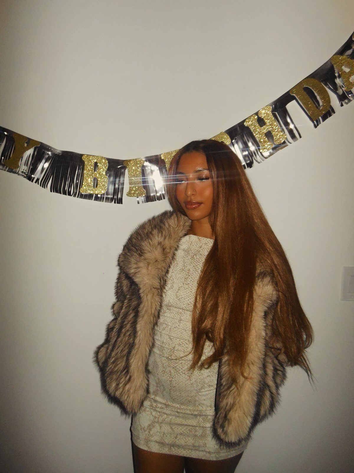 Young woman wearing a brown faux fur coat over a light mini dress.