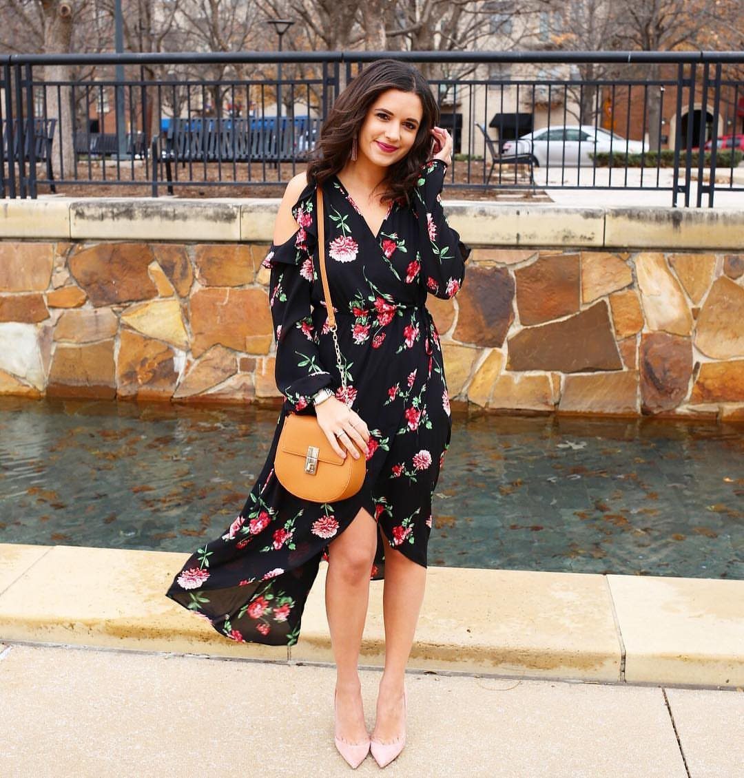 Woman wearing a black floral maxi dress with a tan crossbody bag and heels.