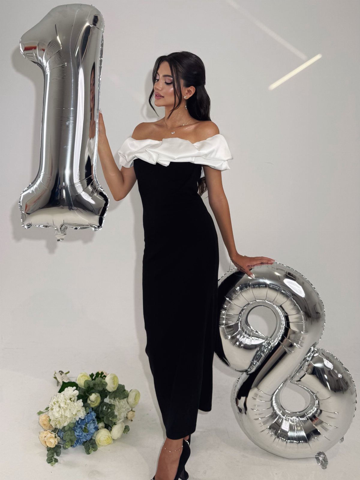 Woman in black and white dress posing with silver 18 balloons and flowers.