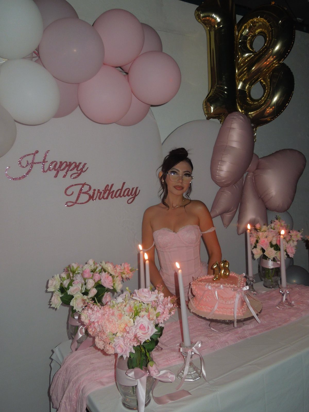 Young woman in pink dress celebrating 18th birthday with cake and balloons