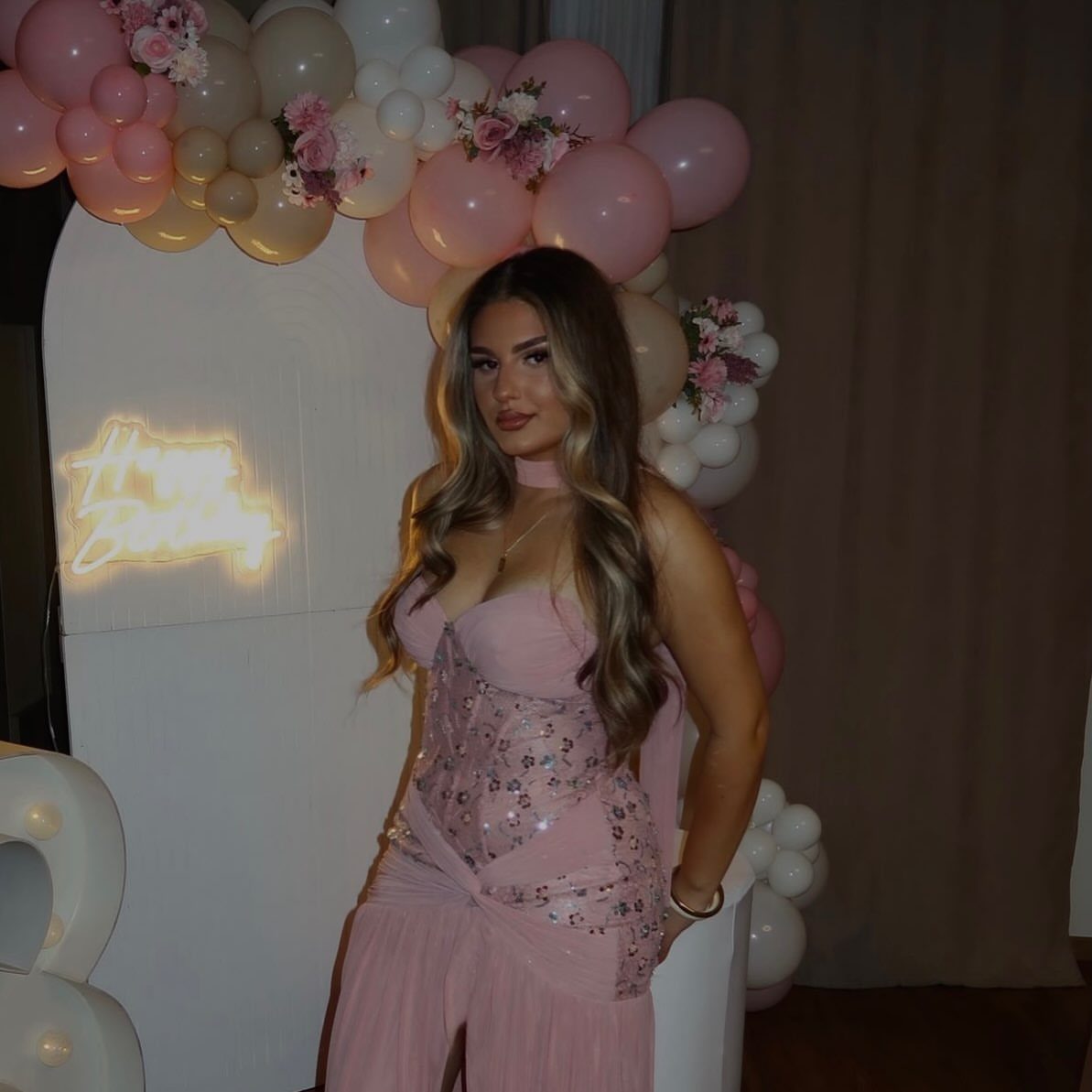 Woman in pink sequined corset top and trousers posing by balloon arch.