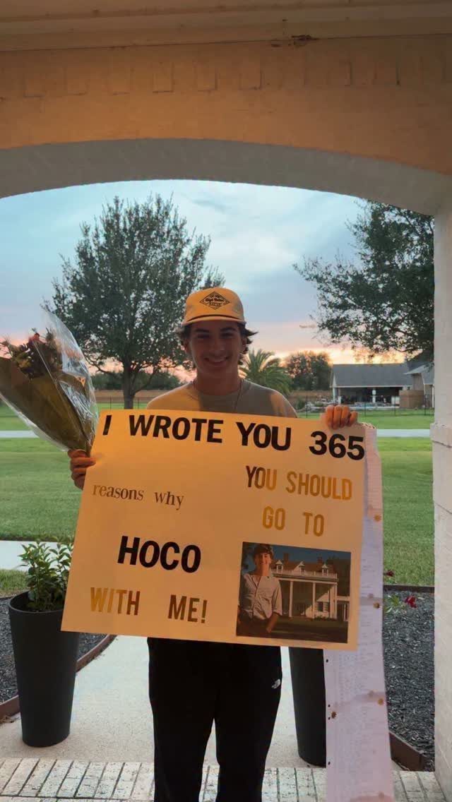 Teenage boy holding a large yellow homecoming proposal sign and a flower bouquet.