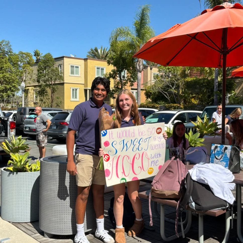 Teenage couple posing with a colorful handmade homecoming proposal sign outdoors