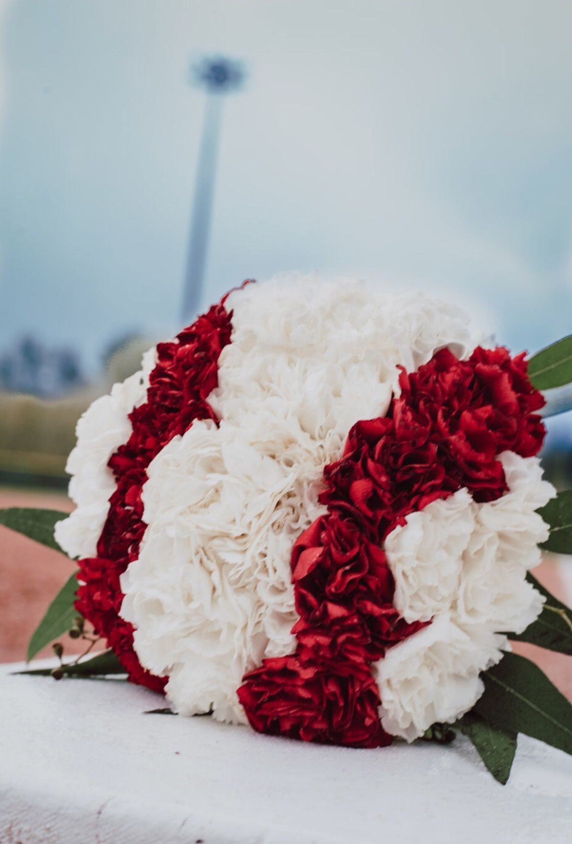 Baseball-shaped floral arrangement of red and white carnations on a white ledge.