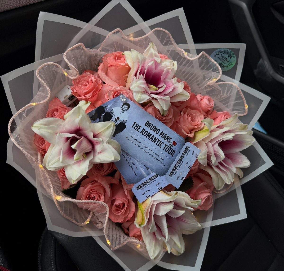 Bouquet of pink roses and lilies with a Bruno Mars concert ticket on top.