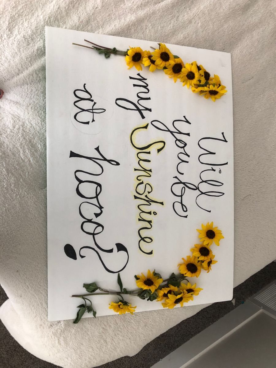 White poster board with faux sunflowers and hoco proposal text on white fabric