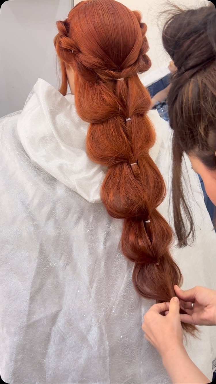 Long red hair styled into a bubble braid by a professional stylist.