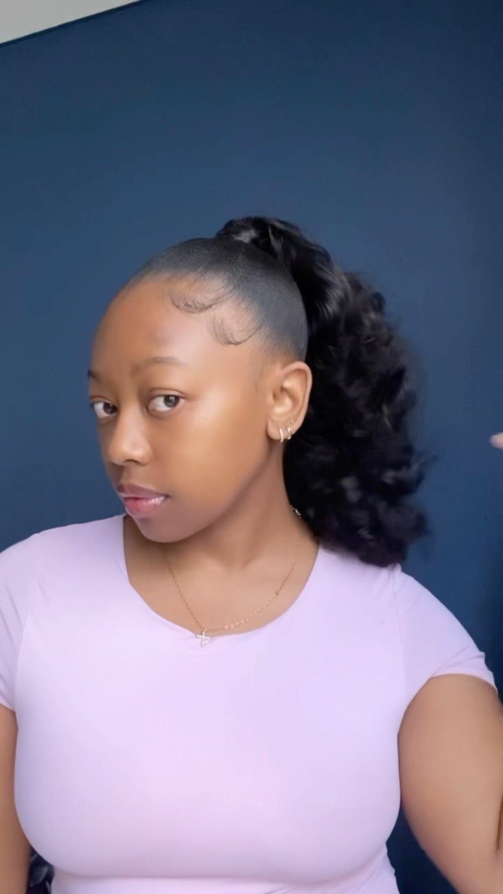 Woman with a high curly ponytail and sleek edges wearing a purple shirt.