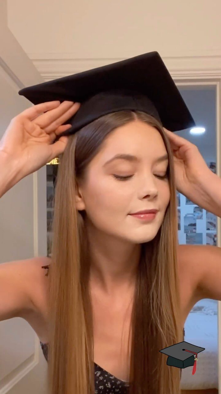Young woman with long straight brown hair putting on a black graduation cap