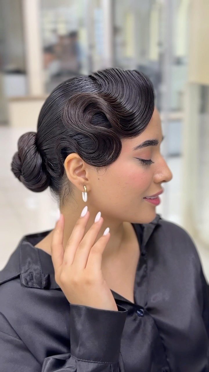Woman with dark hair in a sculpted vintage updo and black satin shirt.