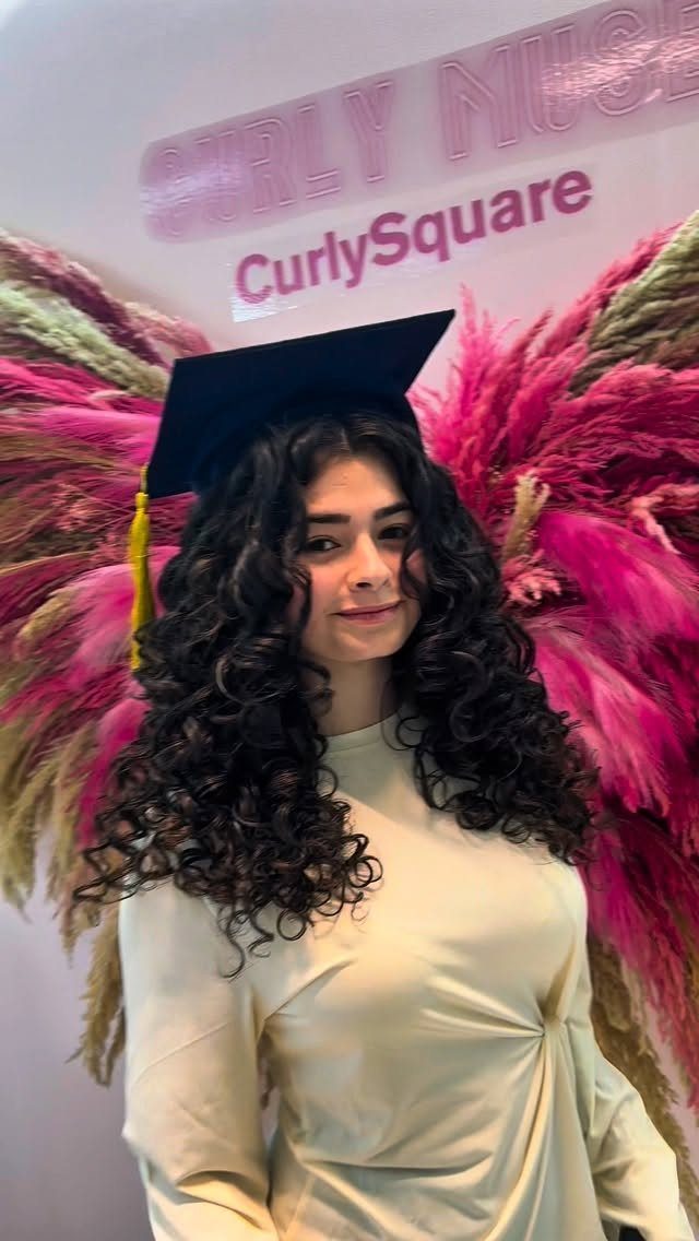 Woman with long natural curls wearing a graduation cap and cream gown.