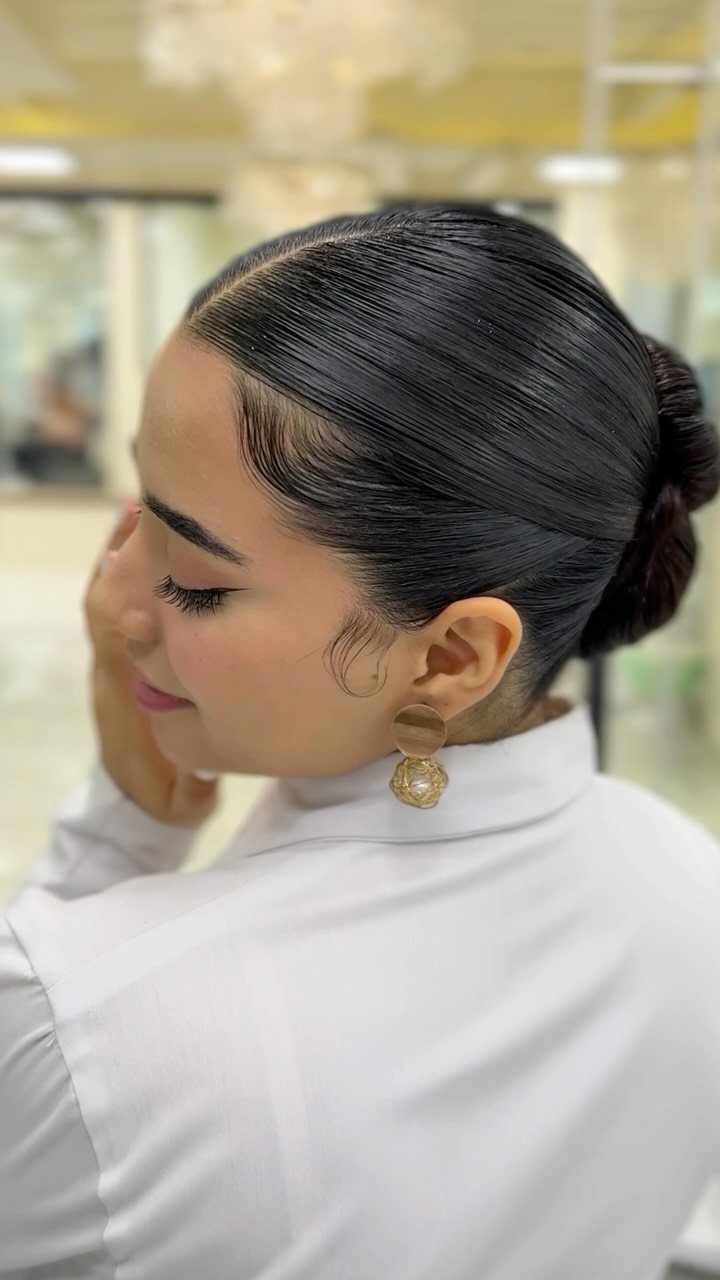 Woman with dark hair in a slicked-back low bun and side part.