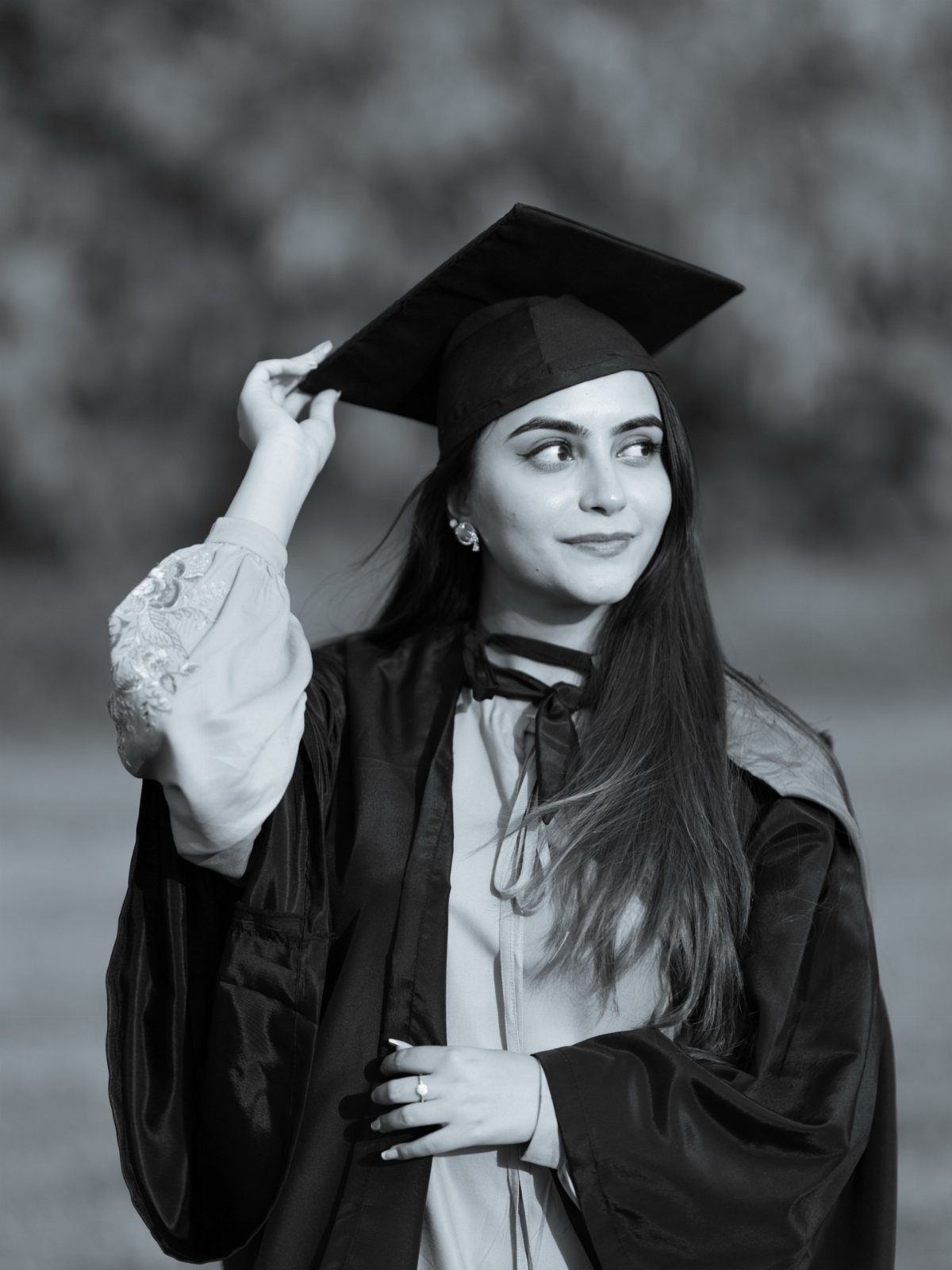 Graduate in cap and gown posing confidently and looking away in black and white.