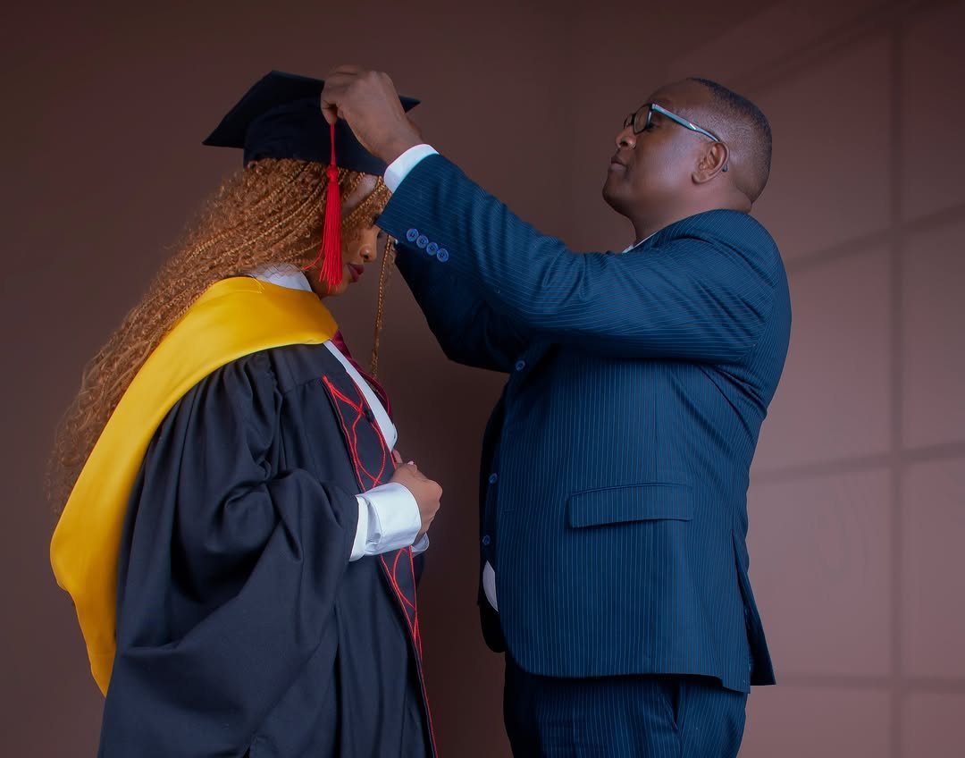 Man in a suit adjusting a graduation cap on a woman in gown