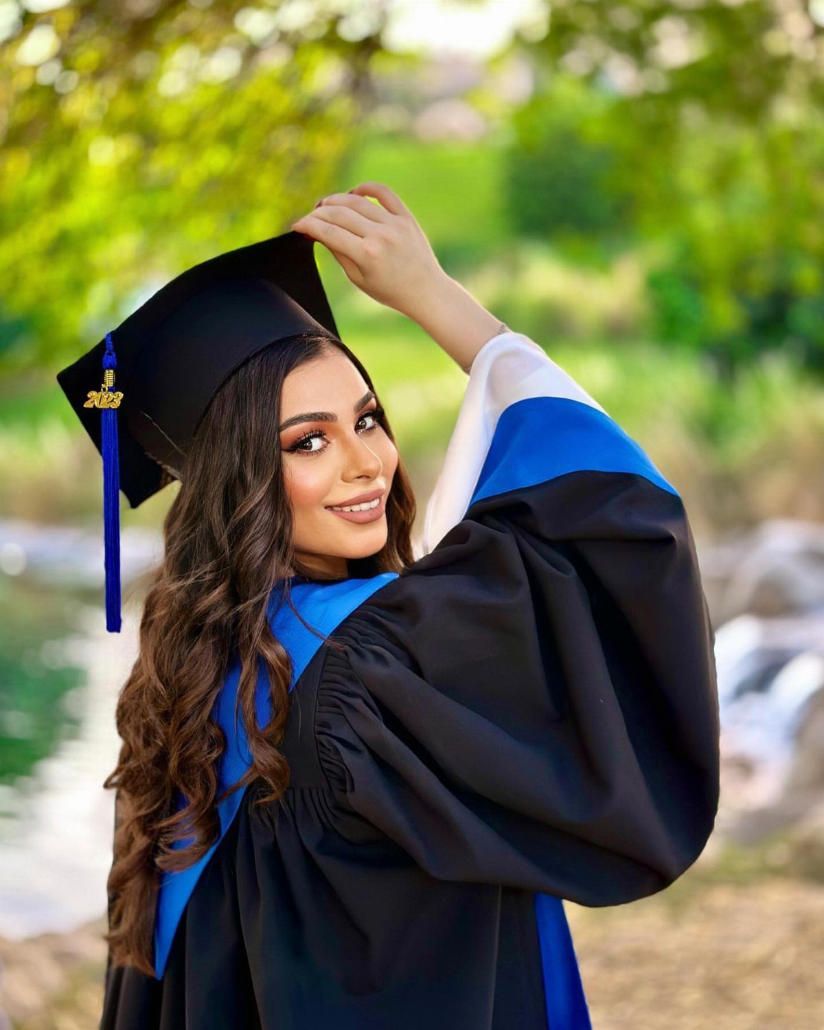 Graduate in black cap and gown posing during golden hour in a park