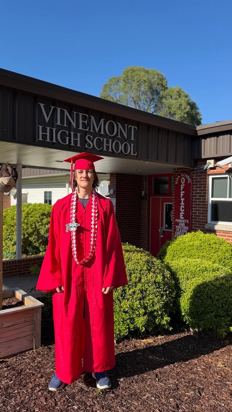 Graduate in red cap and gown posing in front of Vinemont High School sign