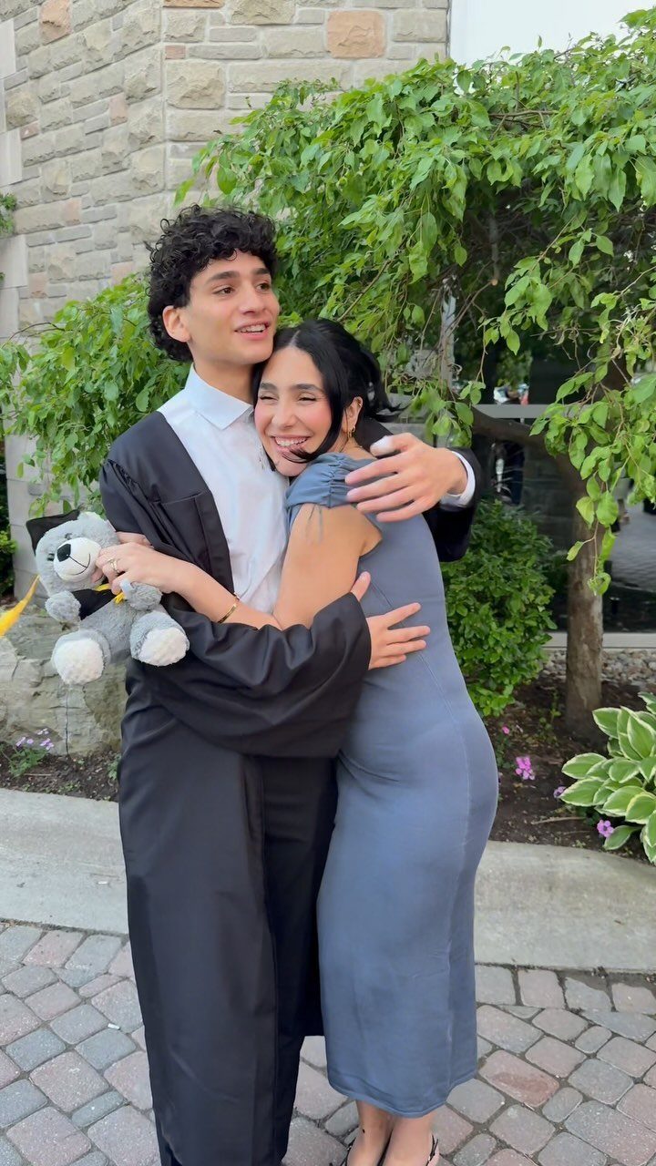 Graduating young man in black gown hugging a young woman in blue dress.