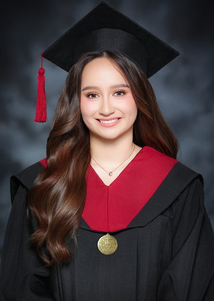 Smiling graduate wearing a black cap and gown with a red stole and tassel.