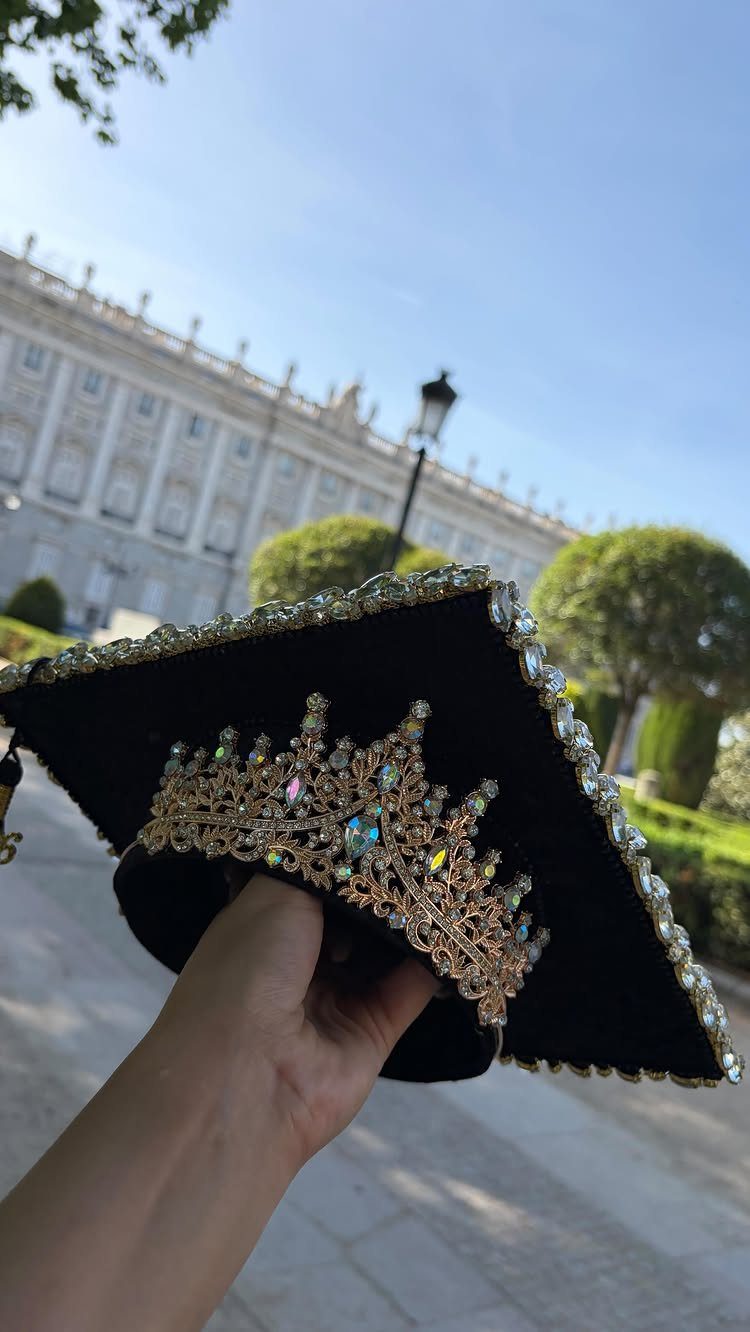 Decorated black graduation cap with a jeweled gold crown held against a palace background