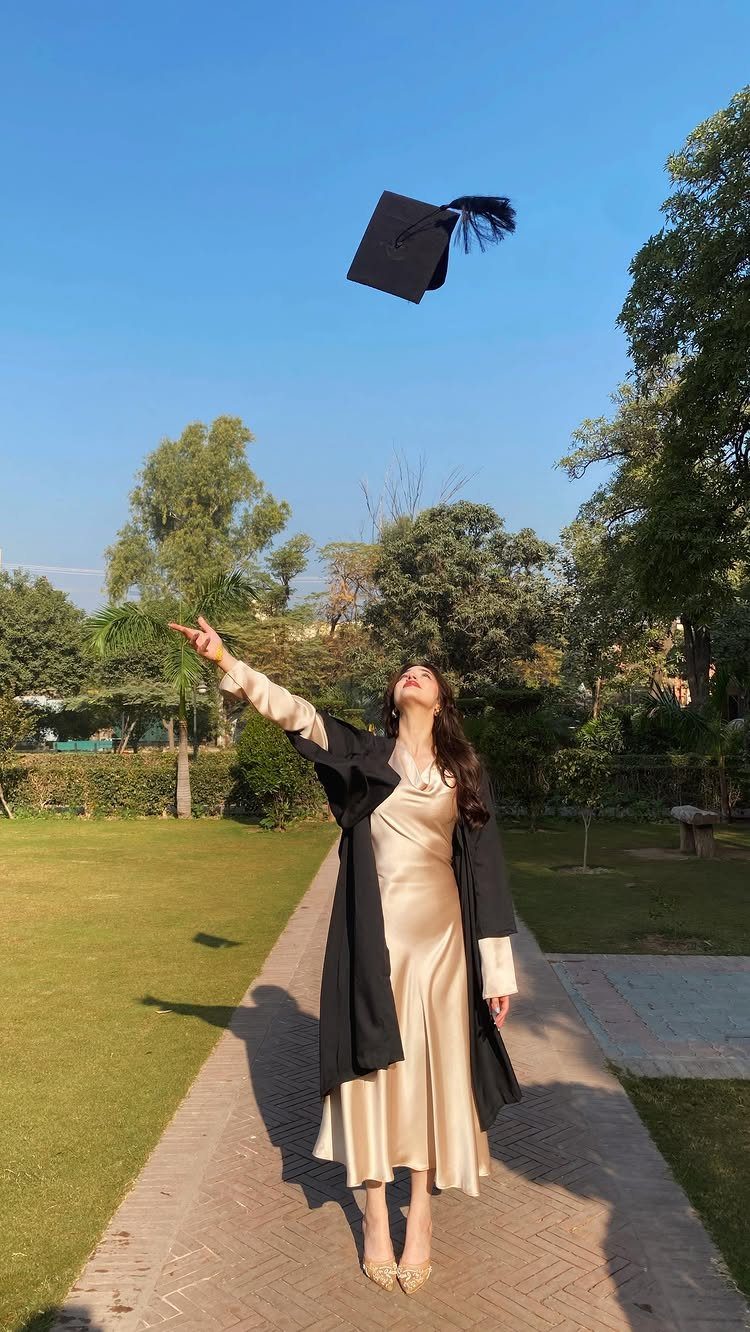 Woman in graduation gown tossing her cap into the air in a sunny park