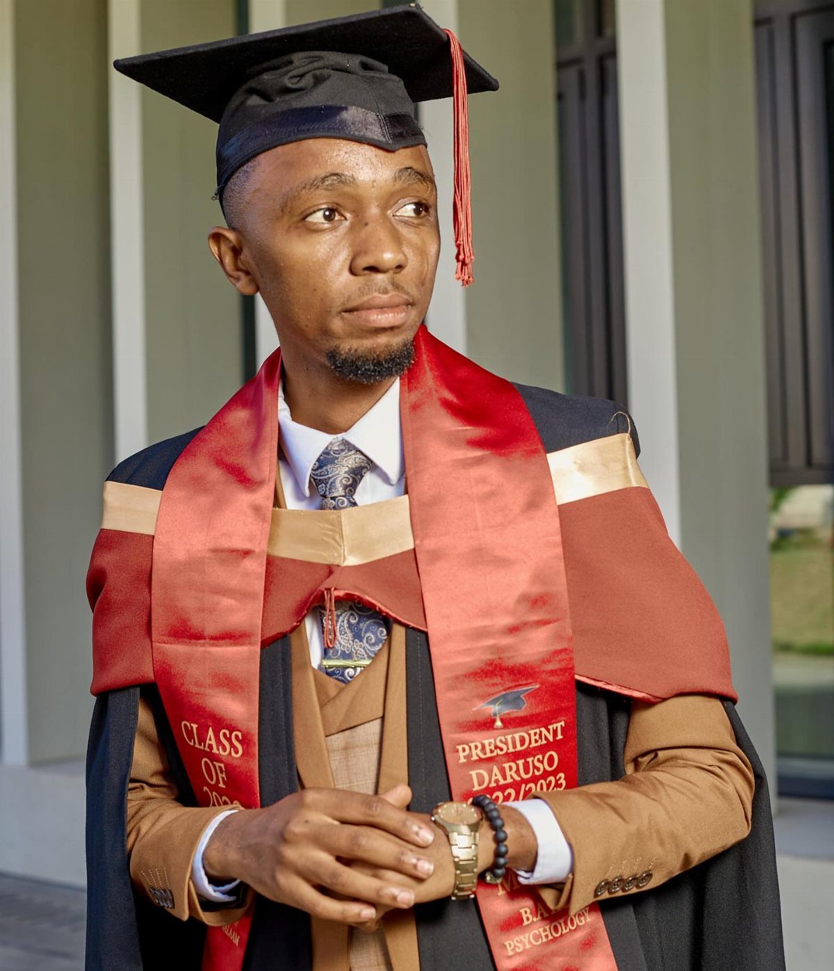 Graduating man in black cap and gown with red and gold stole.