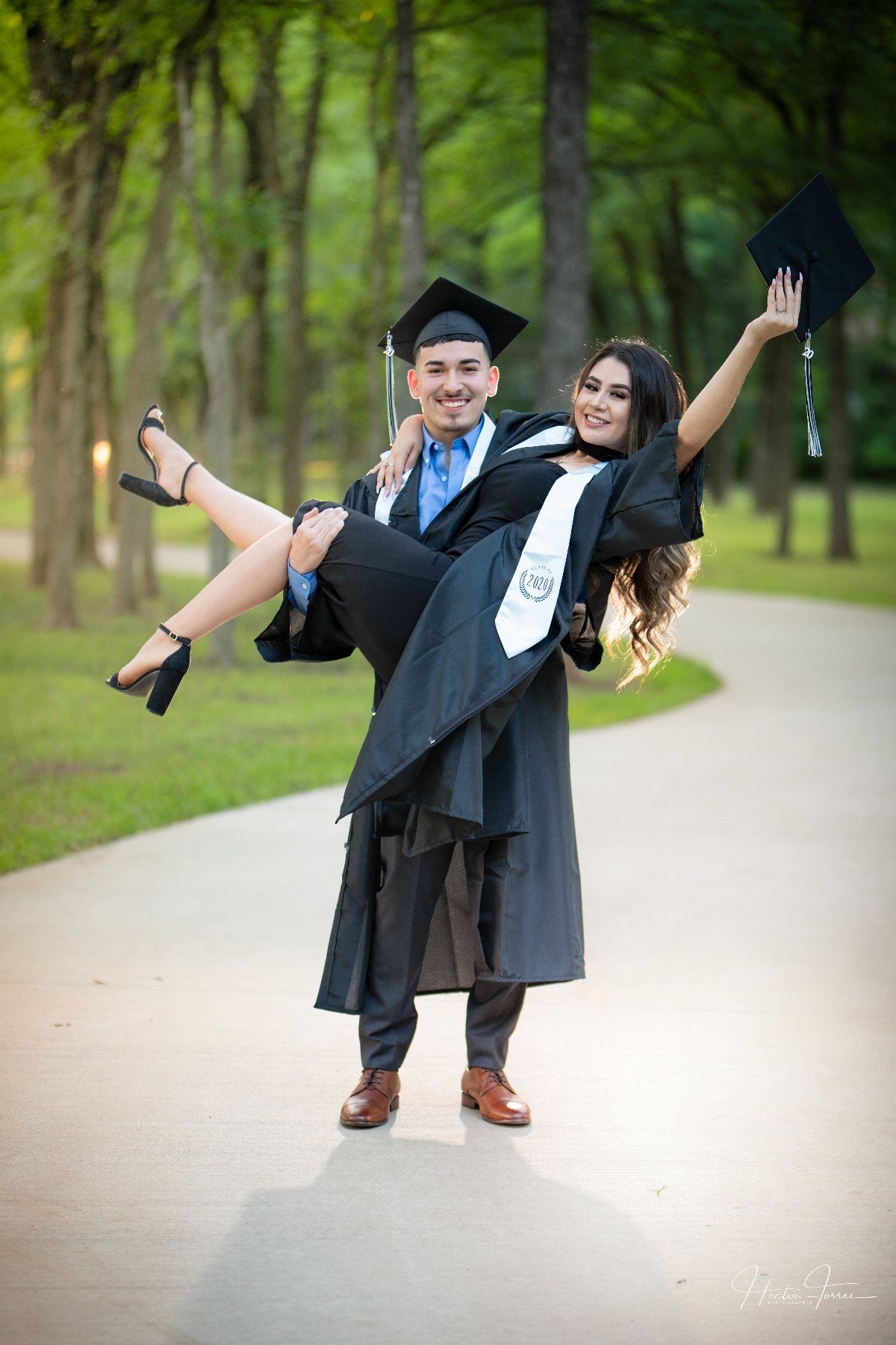 Graduating couple smiling as the man carries the woman on a campus path