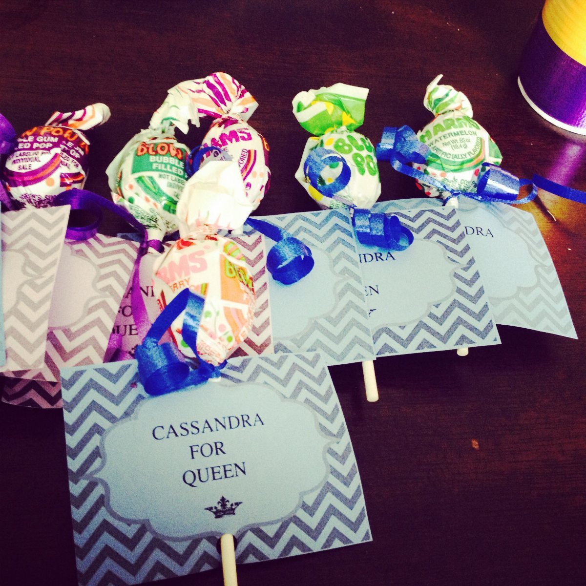 Campaign signs for queen with colorful lollipops tied to them with ribbons.