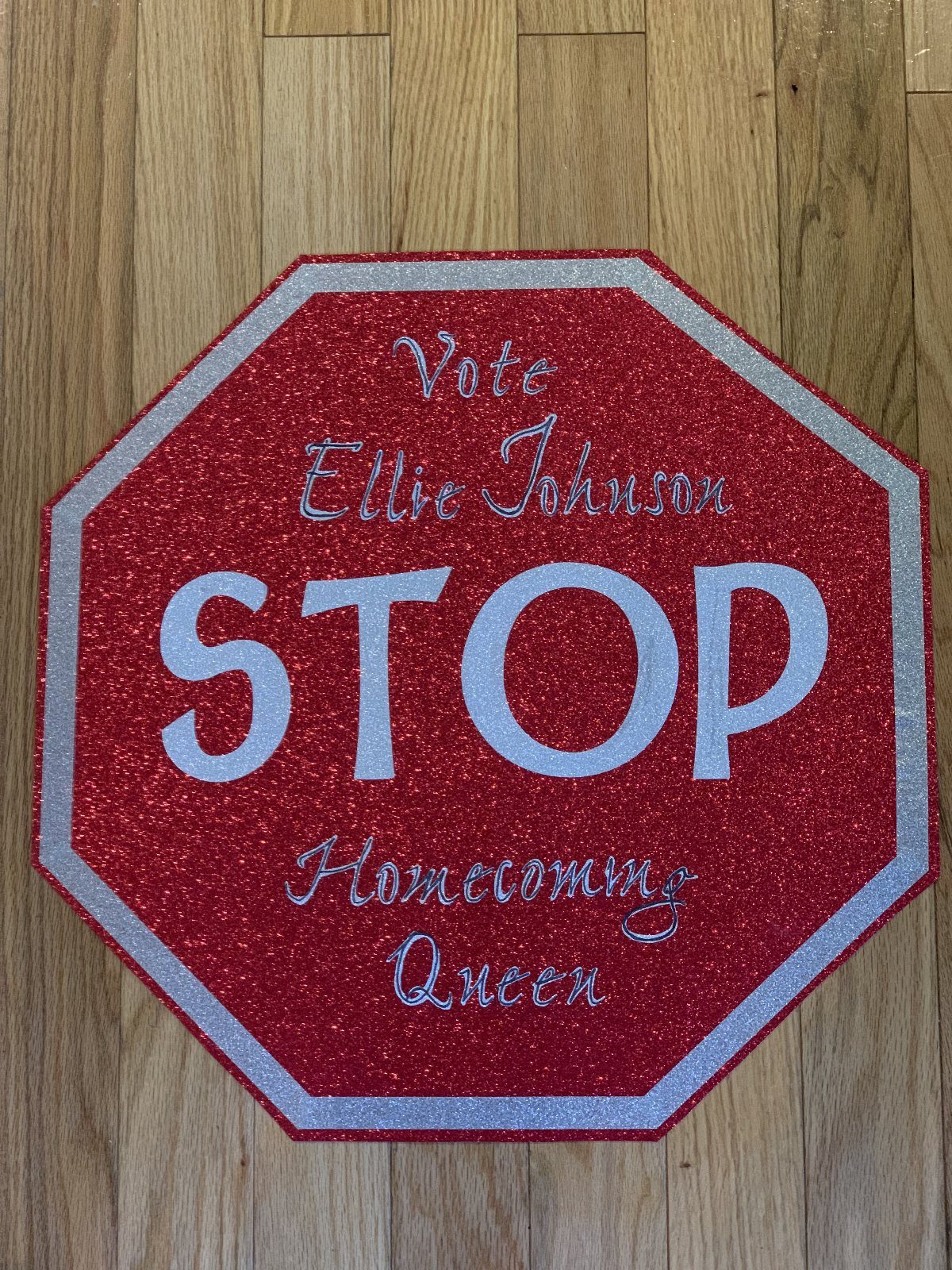 Red glittery stop sign poster for a homecoming queen campaign on wooden floor
