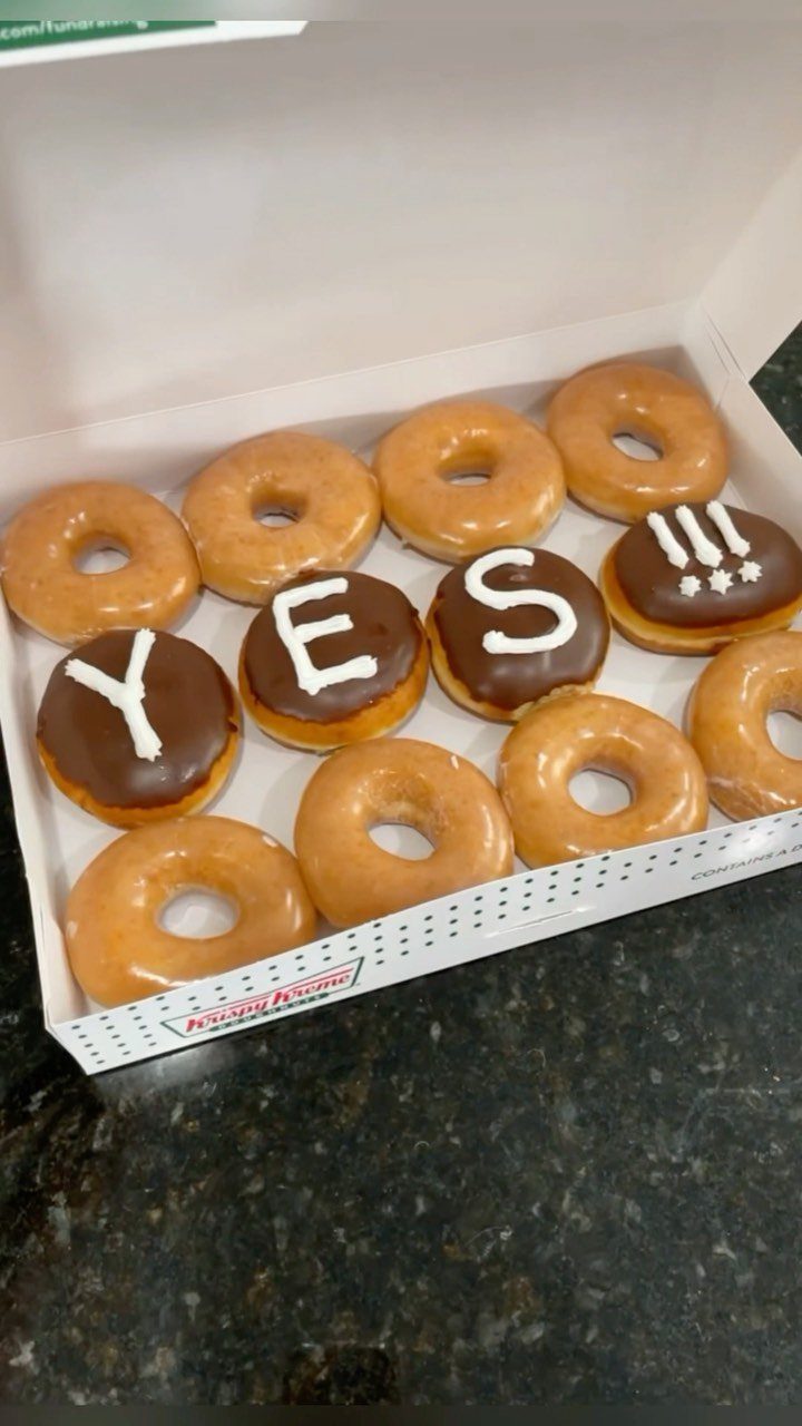 Box of glazed donuts with chocolate donuts spelling out YES in white icing