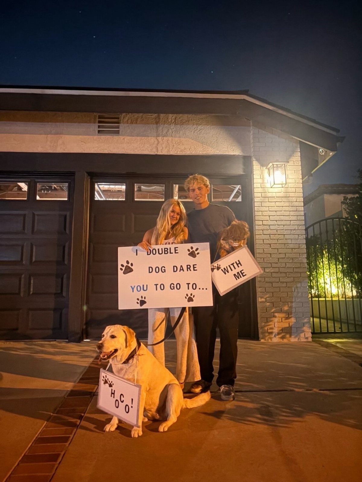 Couple holding a promposal sign with a yellow Labrador wearing a small note.