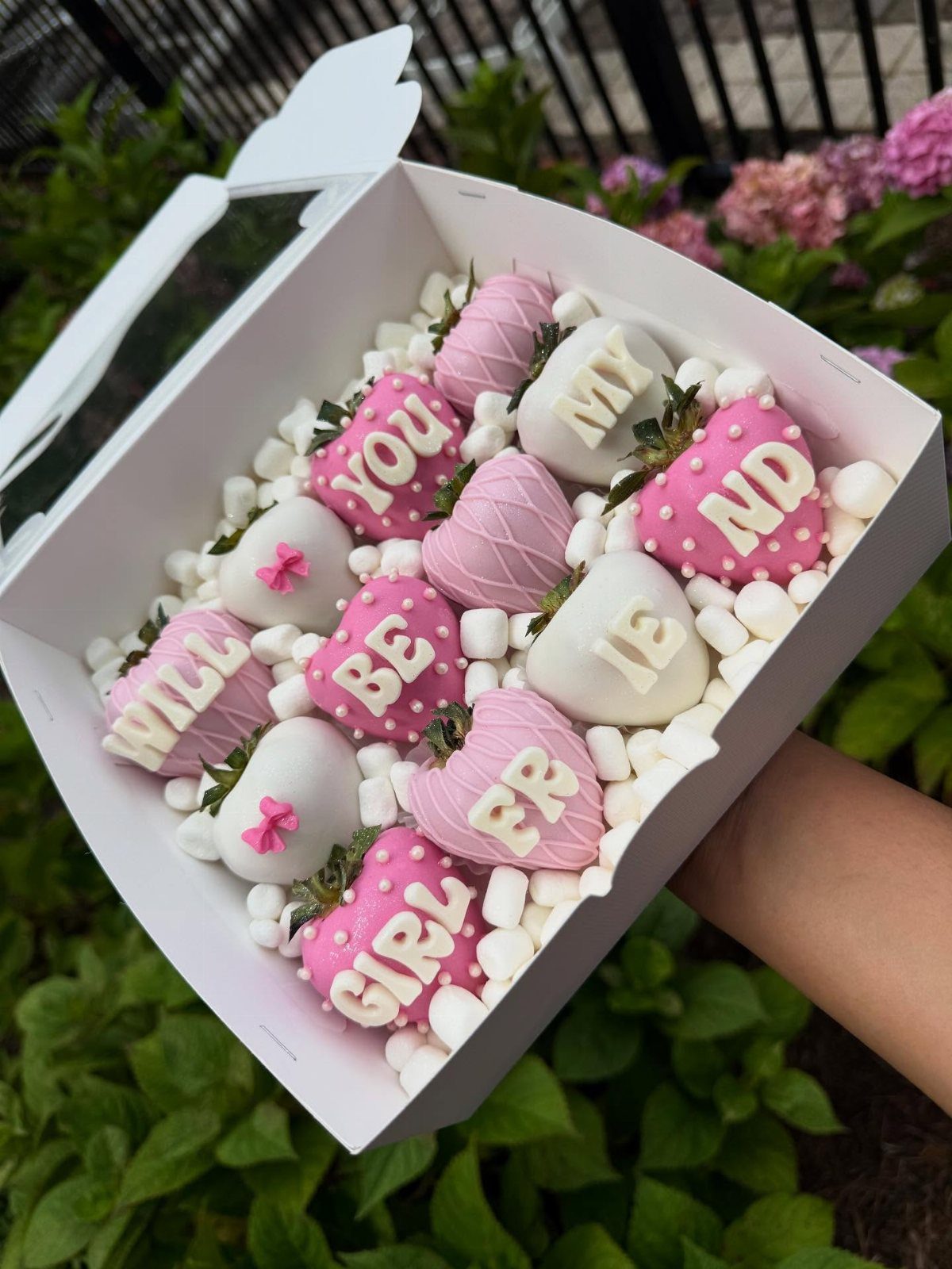 Chocolate-covered strawberries in pink and white with letters in a white gift box.
