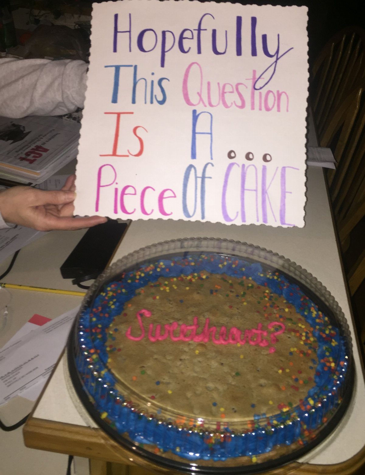 Large round cookie with sprinkles and a colorful promposal poster on a table