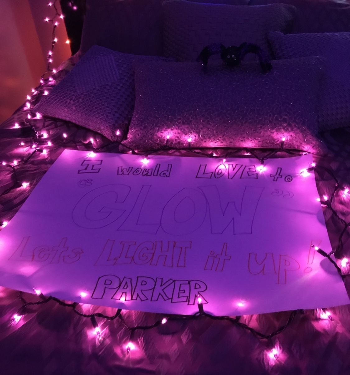 Hand-drawn promposal poster with purple text surrounded by glowing pink fairy lights on bed