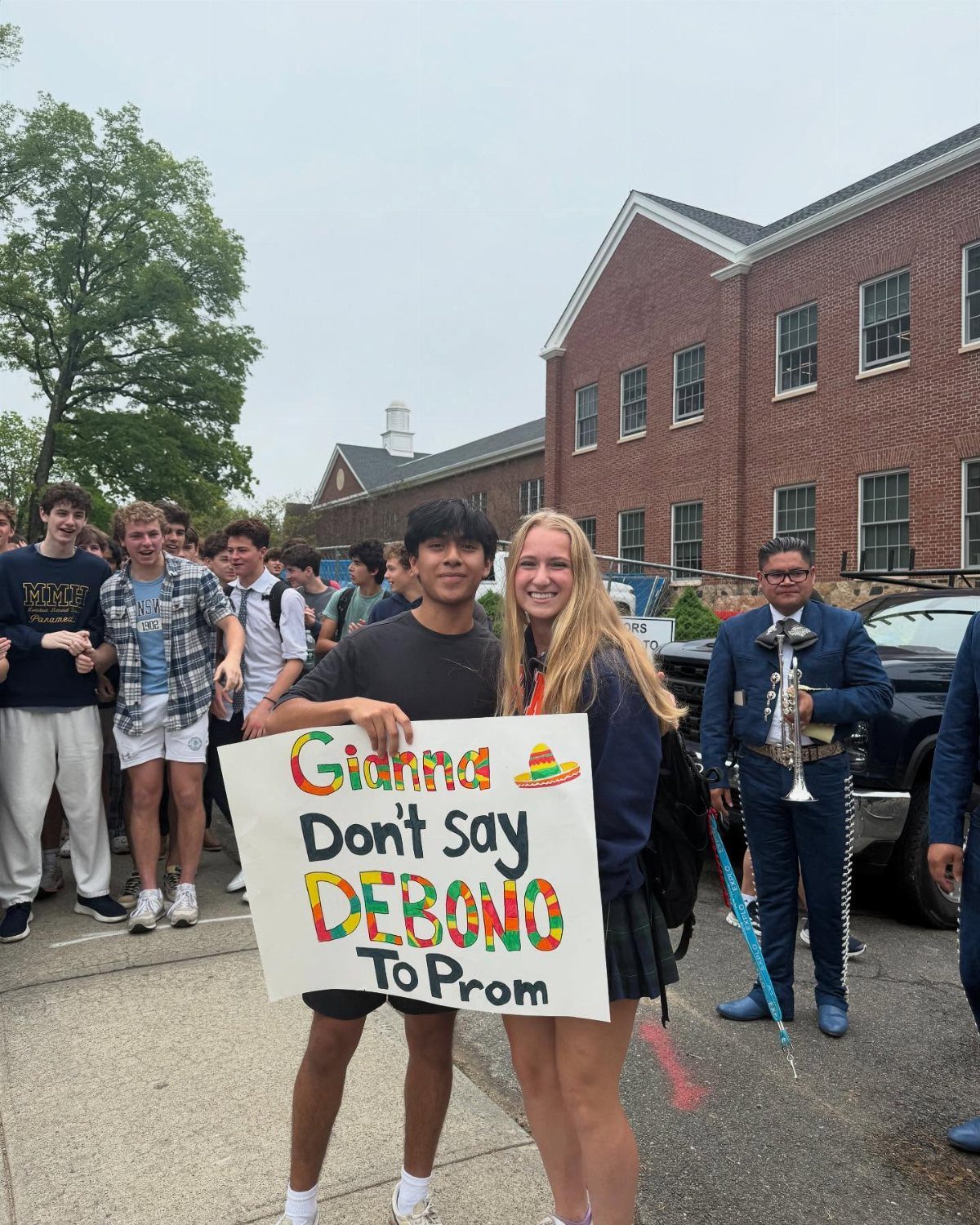 Teenagers holding a promposal poster with a trumpet player in a blue suit.