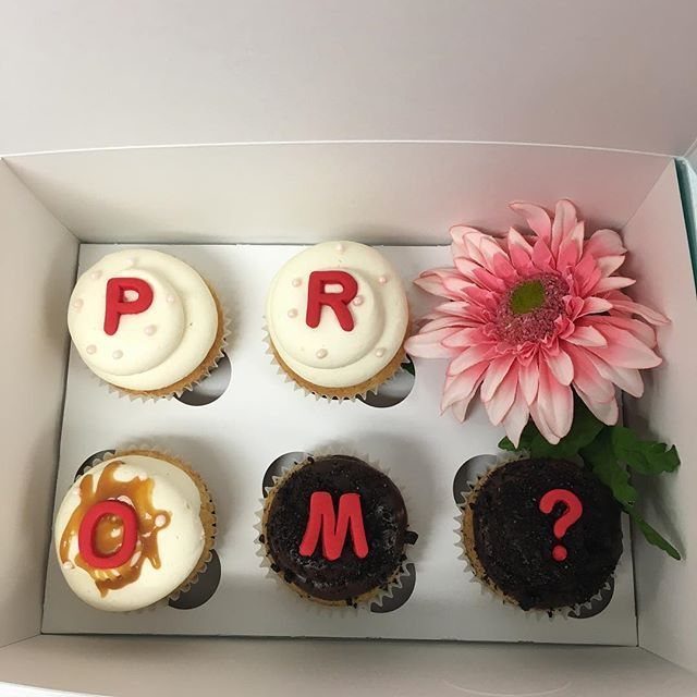 Cupcakes in a white box spelling PROM? with a pink flower beside them.