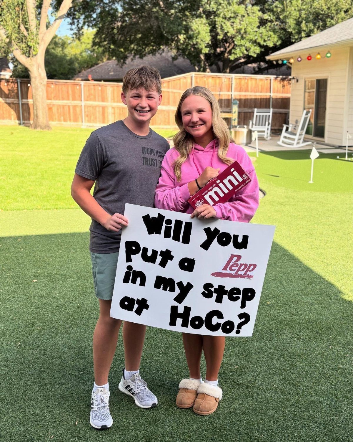 Teenage couple holding a homecoming proposal sign and a red Pepp product outdoors.