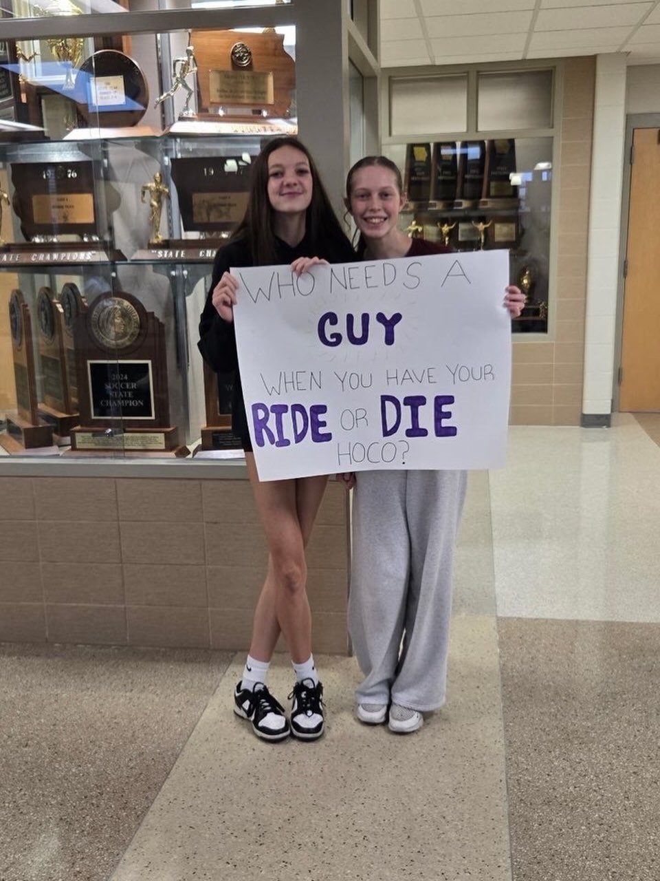 Two teenage girls holding a homecoming proposal poster for a best friend.
