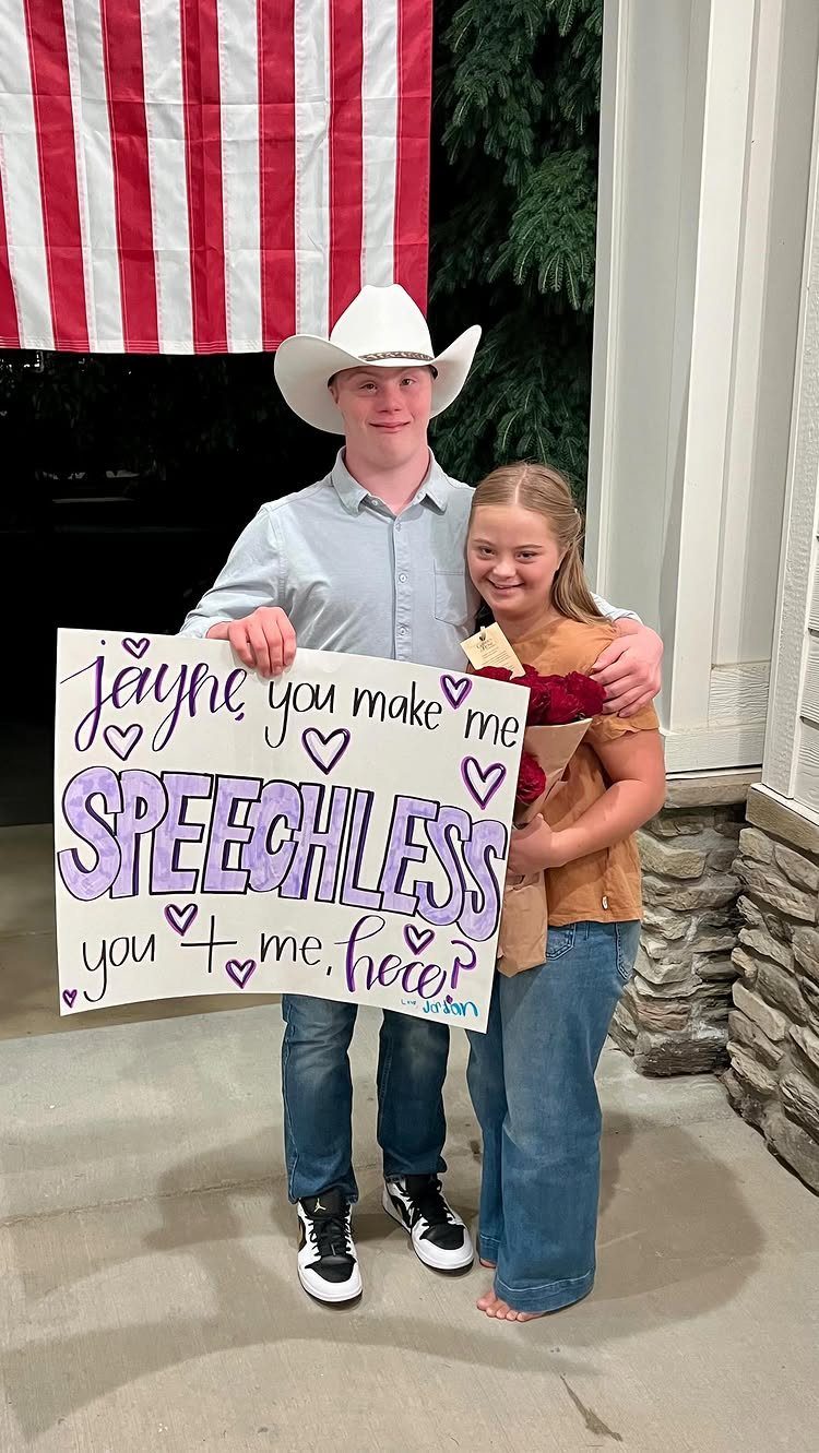 Teenage boy holding a homecoming proposal poster while standing with a teenage girl.