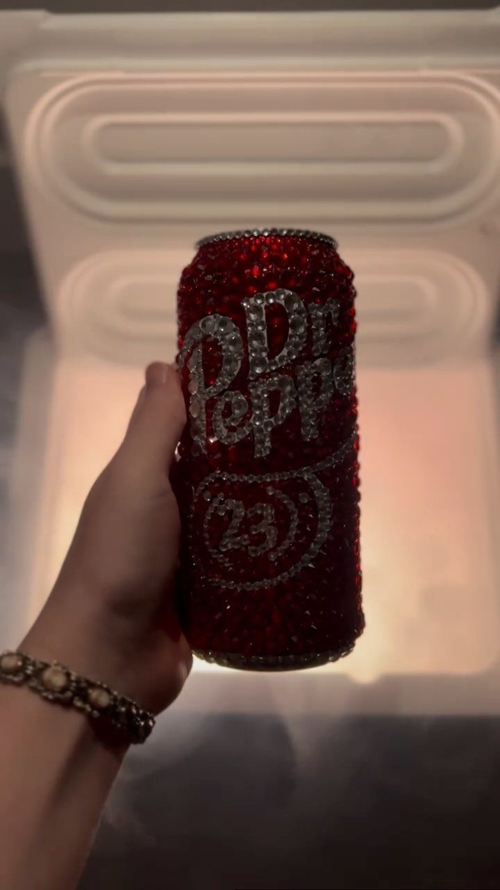 Rhinestone covered red Dr Pepper can held by a hand against white background