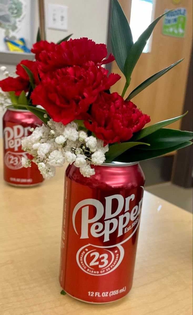 Red Dr Pepper cans used as vases for red carnations and baby's breath.