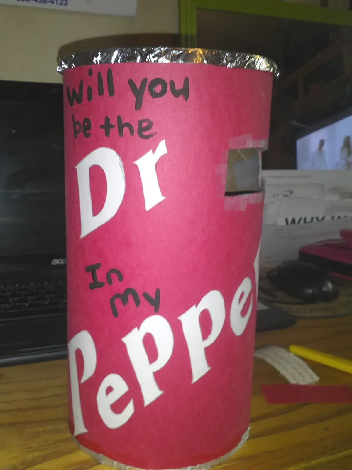 Red cylindrical container with Dr Pepper prom proposal text on a wooden desk