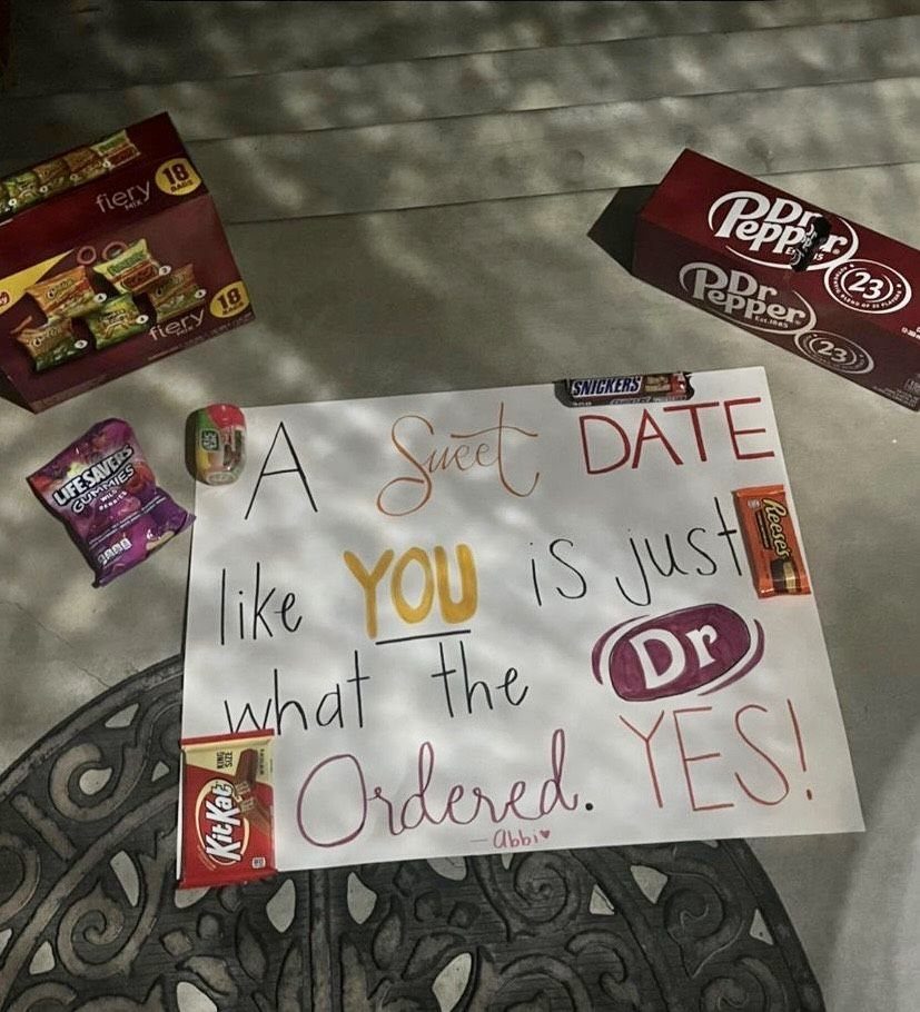 Handwritten prom proposal sign surrounded by Dr Pepper soda and various candy bars.
