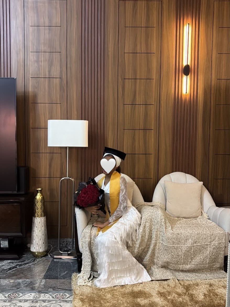 Woman in white gown and graduation cap sitting on a white sofa