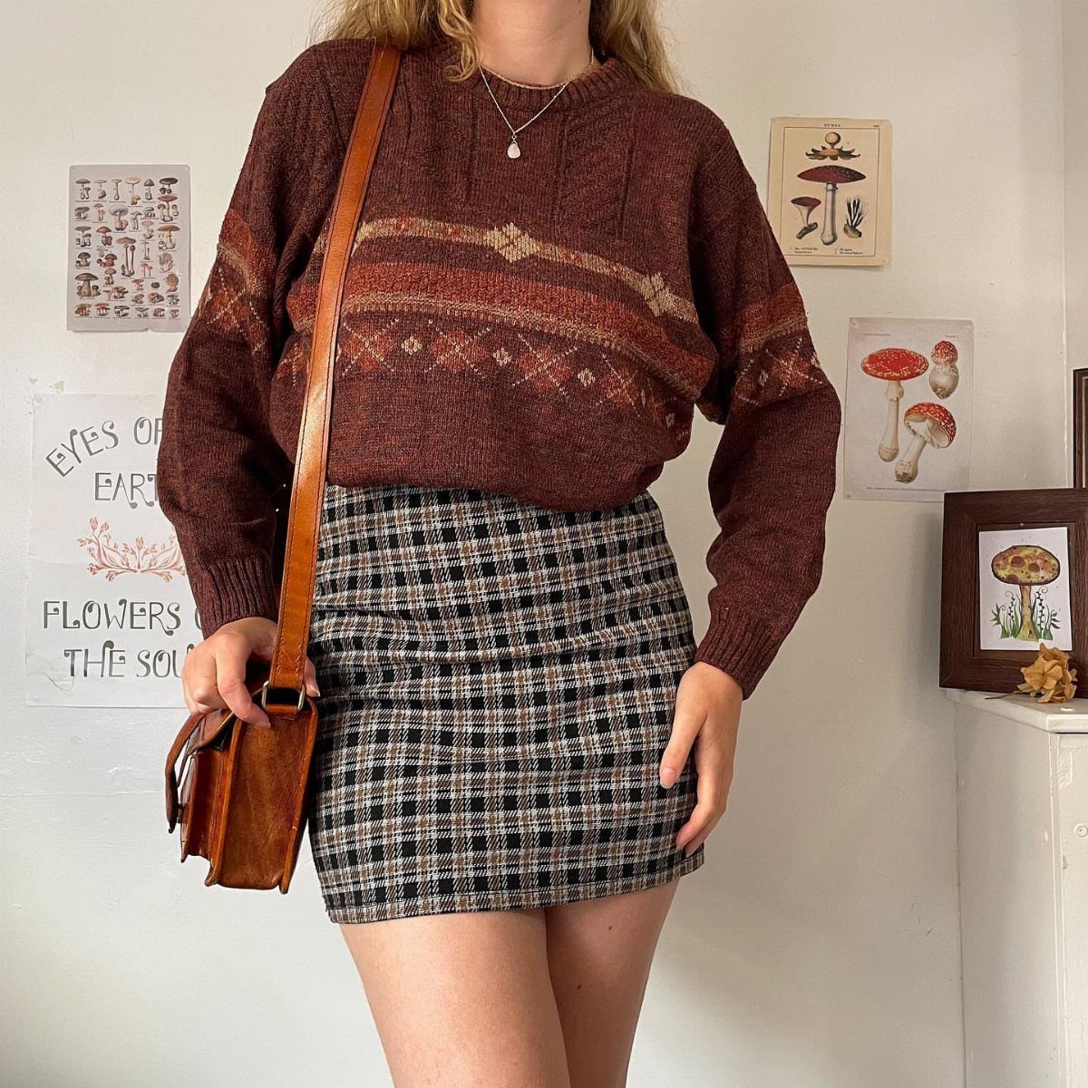 Person wearing a brown patterned cozy sweater and plaid mini skirt with leather bag.