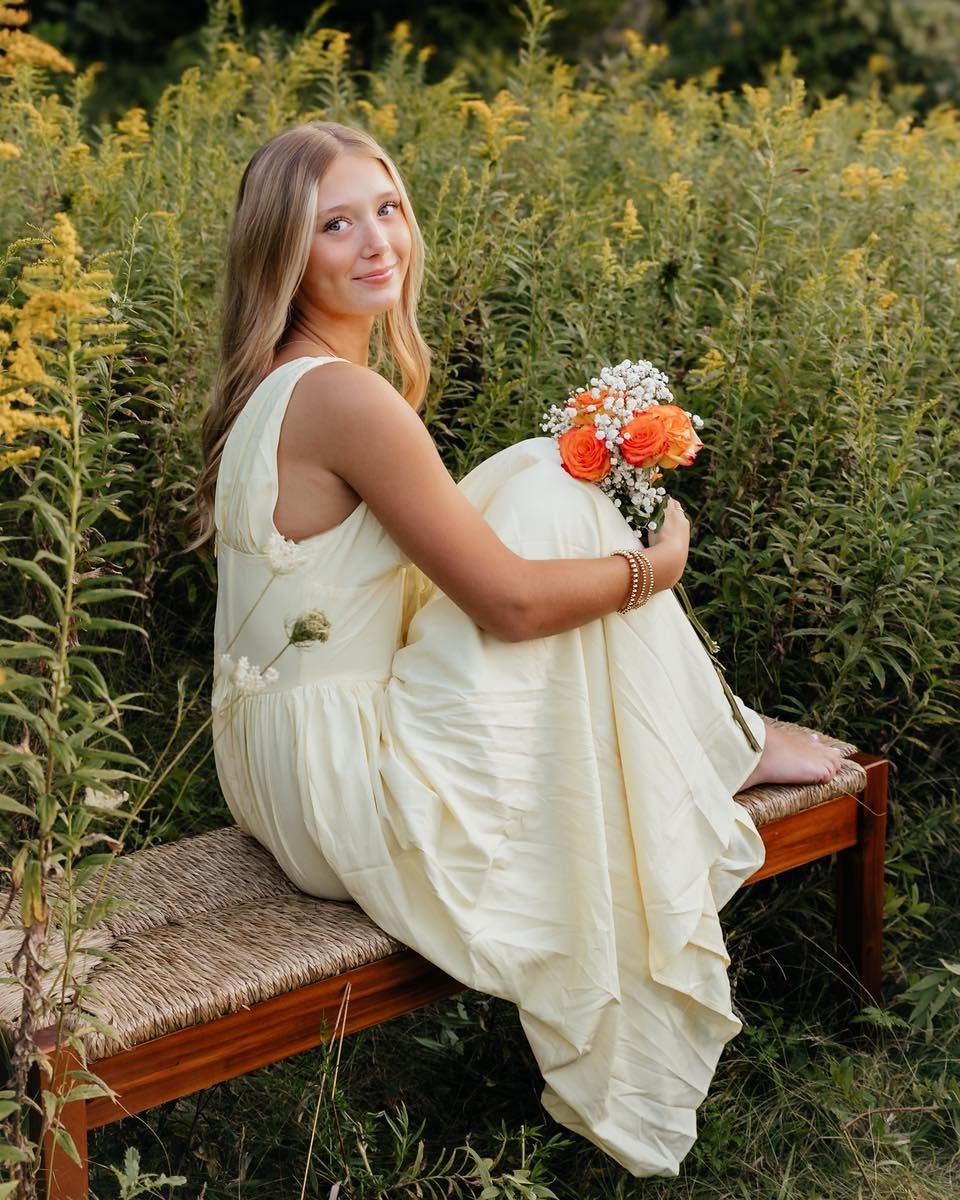 Young woman in a cream flowy dress holding orange roses in a wildflower field