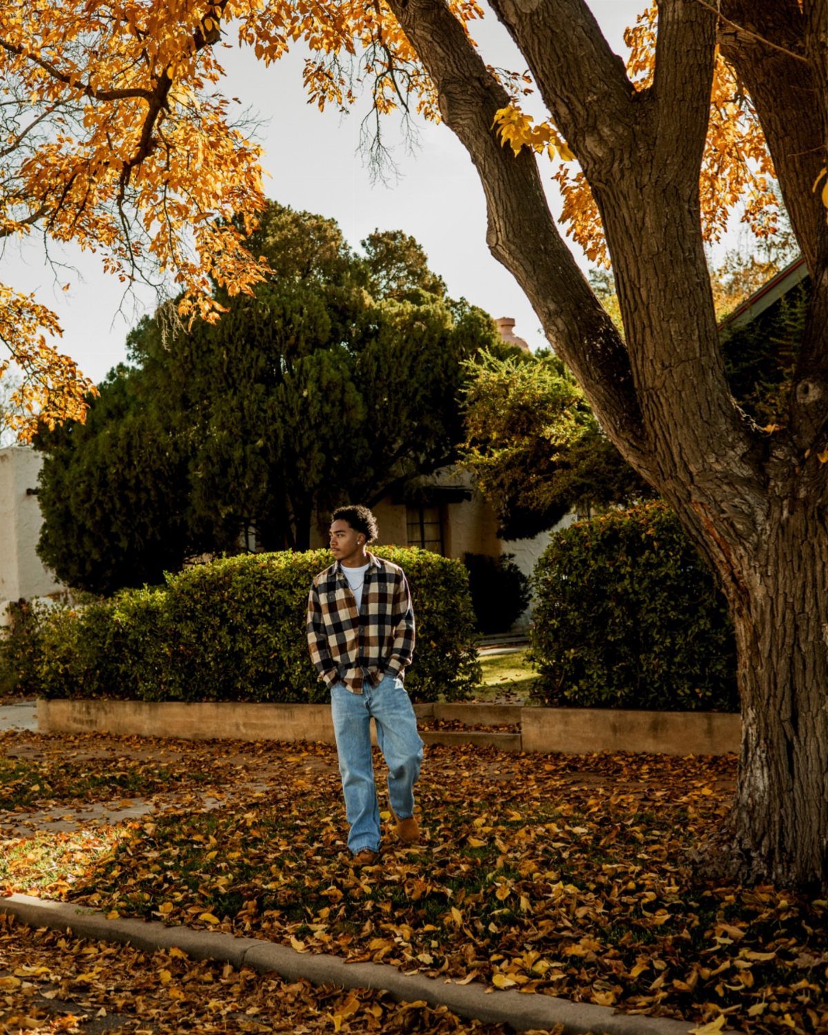 Young man wearing a red plaid flannel shirt and jeans among autumn leaves.