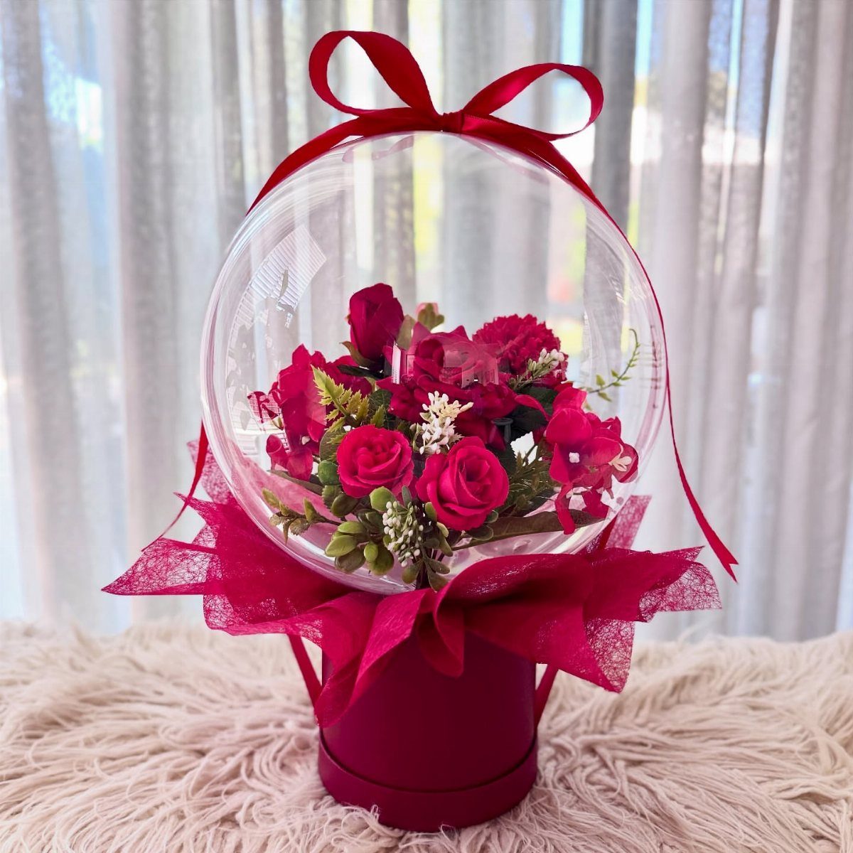 Clear balloon filled with red roses sitting on a red gift box.