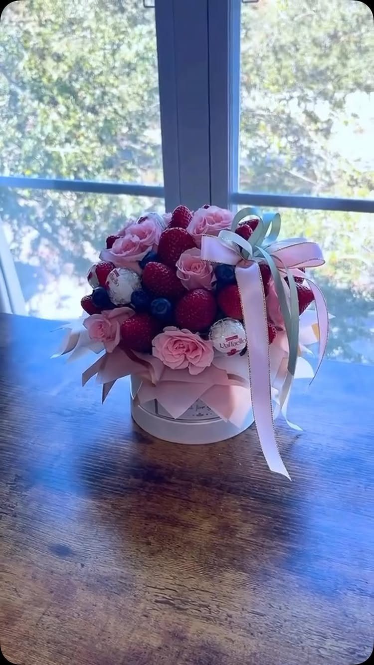 Edible bouquet of pink roses, strawberries, and blueberries in a white box.