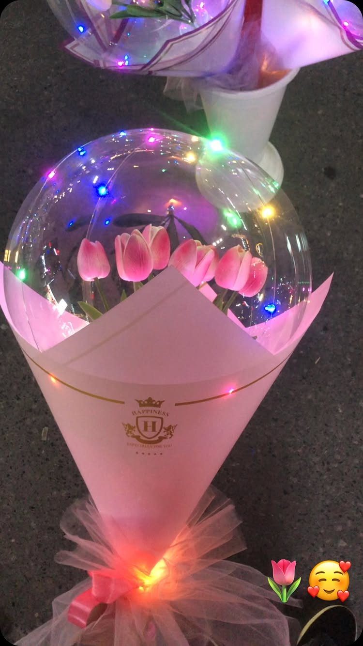 Pink tulips inside a clear balloon with colorful fairy lights and pink wrapping.