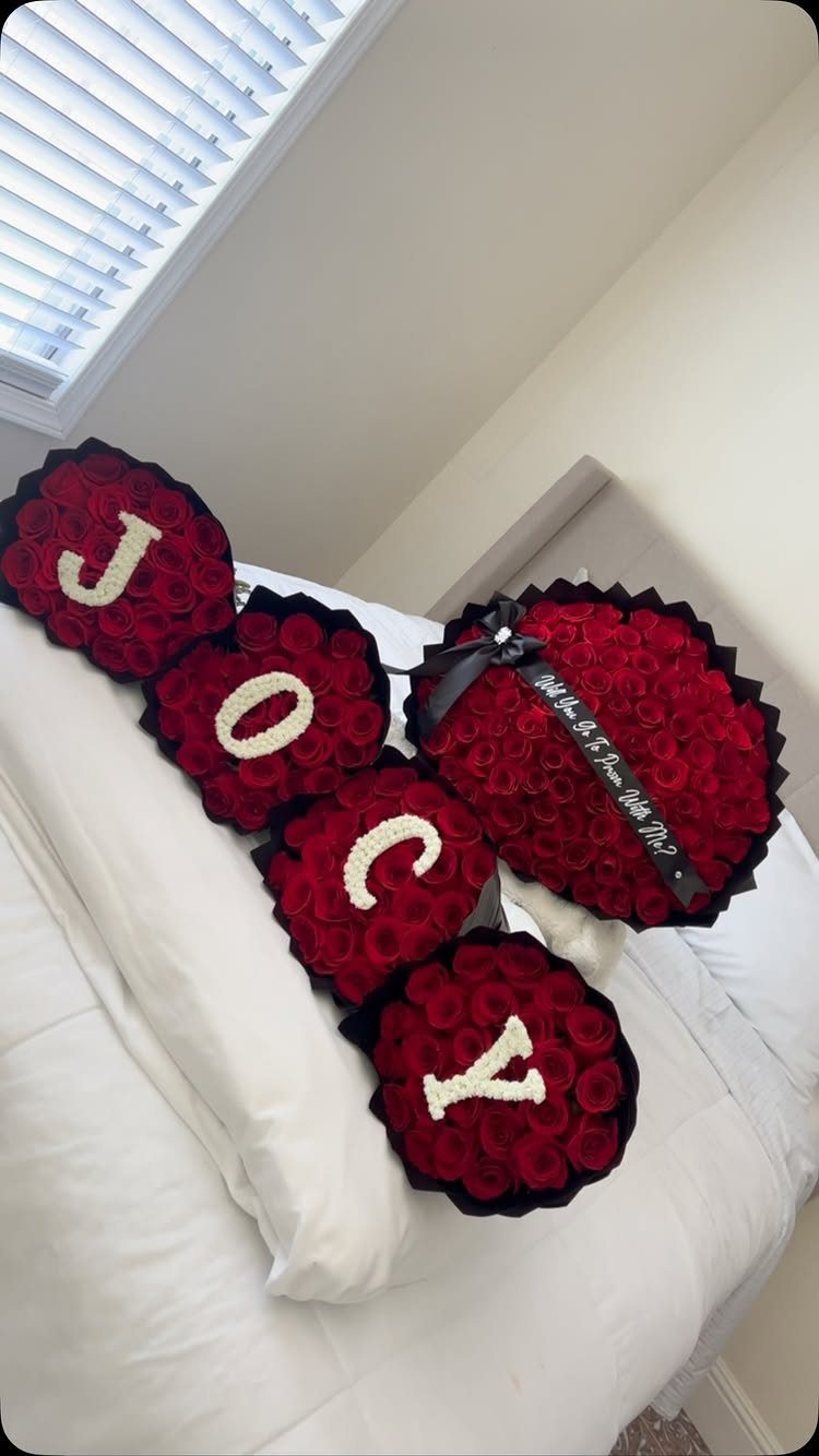 Red rose heart boxes spelling JOCY and a larger rose heart on a bed